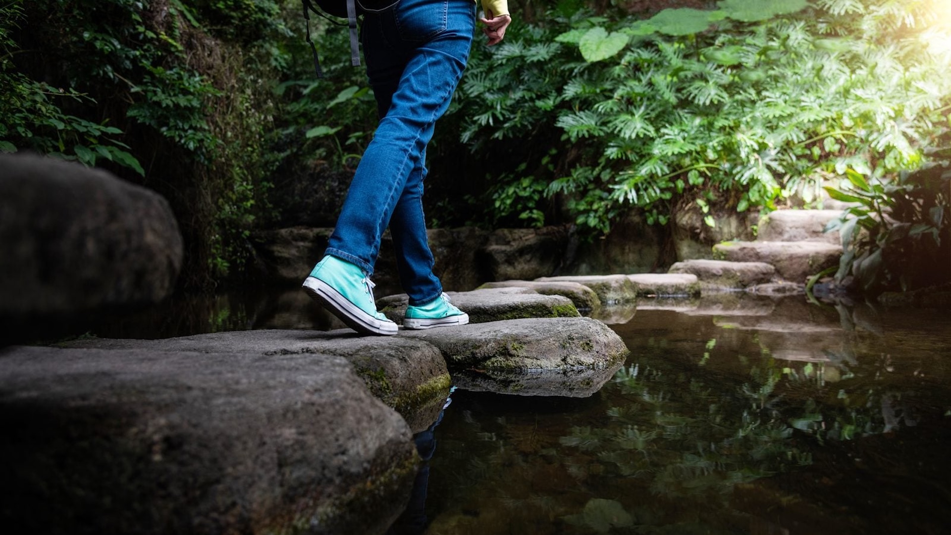 person walking in the forest along a log across a creek
